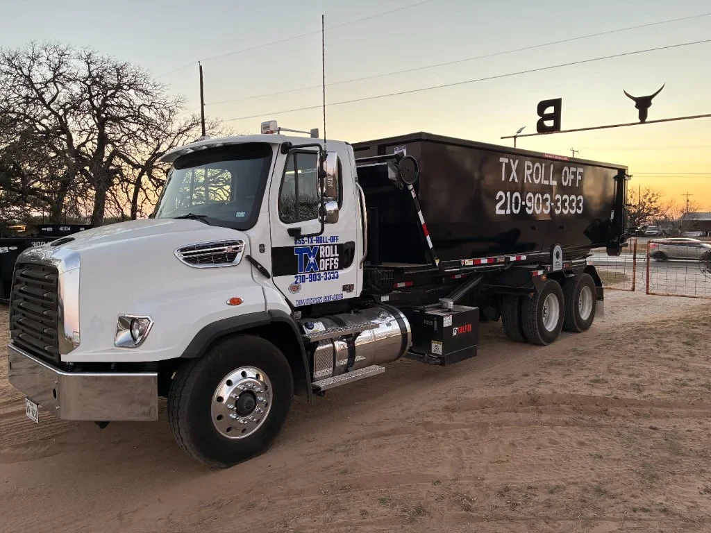 White Freightliner truck with black steel roll-off dumpster container and dual rear axles