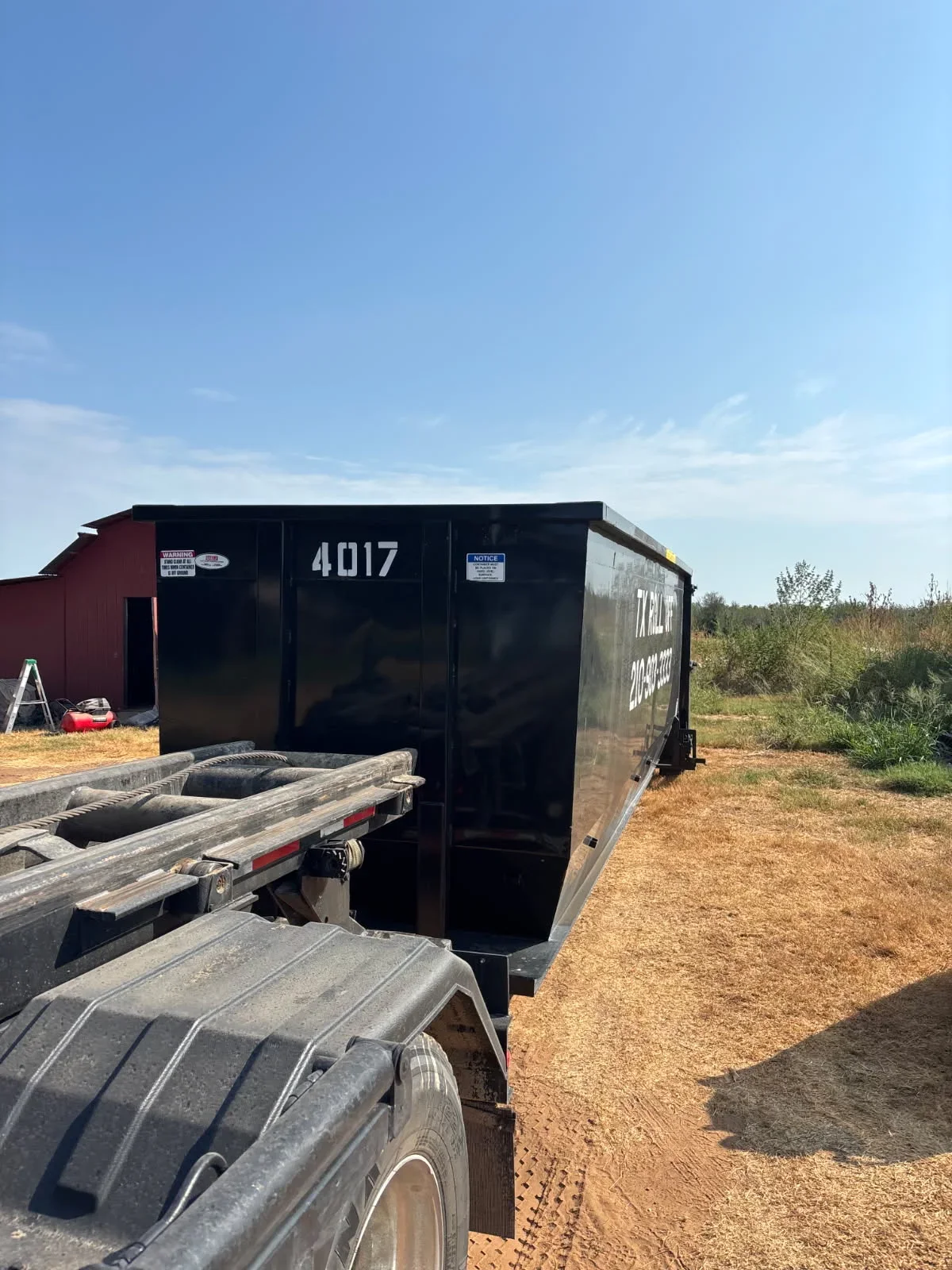 Black roll-off dumpster with enclosed design and locking doors positioned on dirt ground
