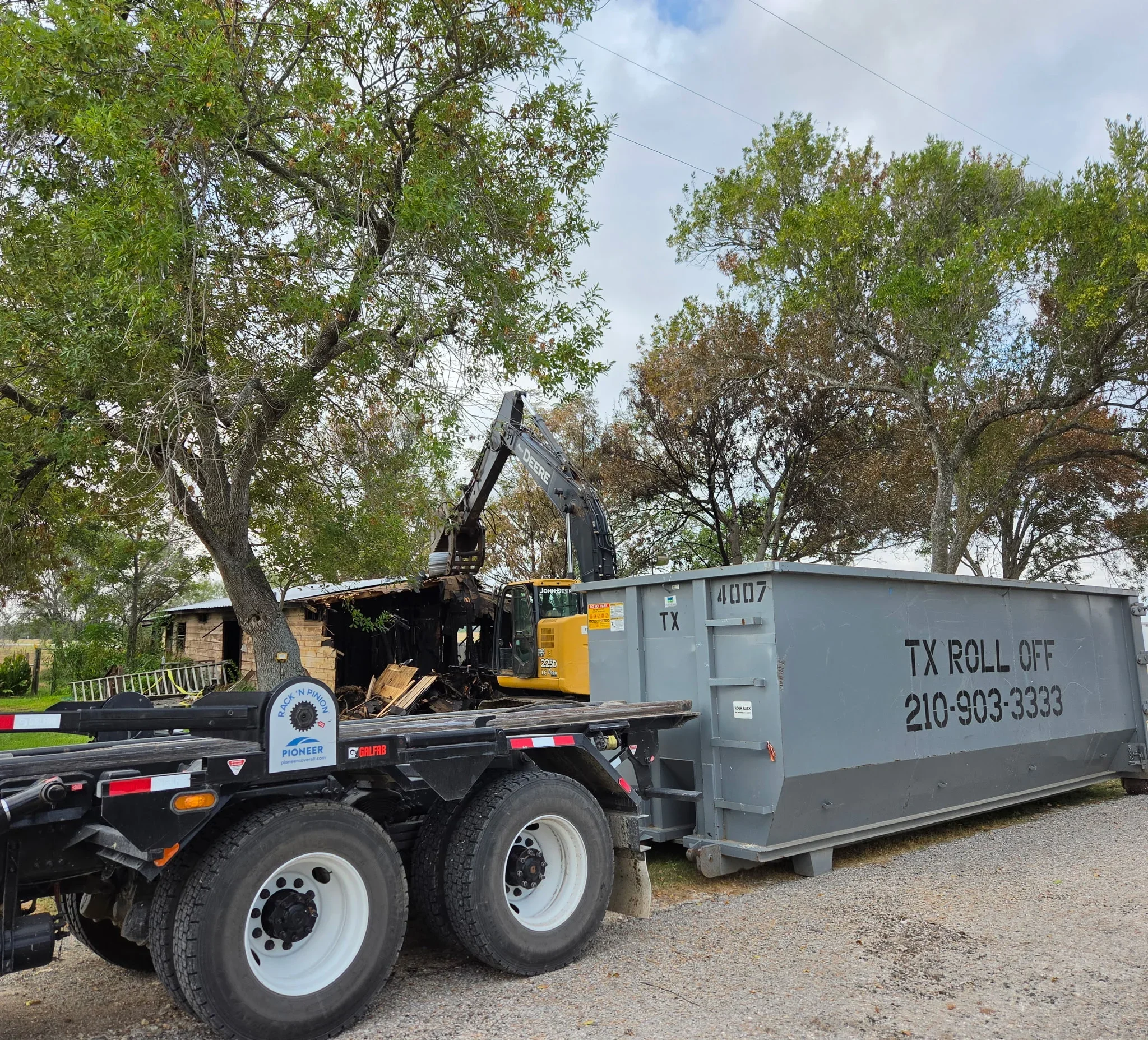Hydraulic arm truck loading demolished wood debris into gray roll-off dumpster container
