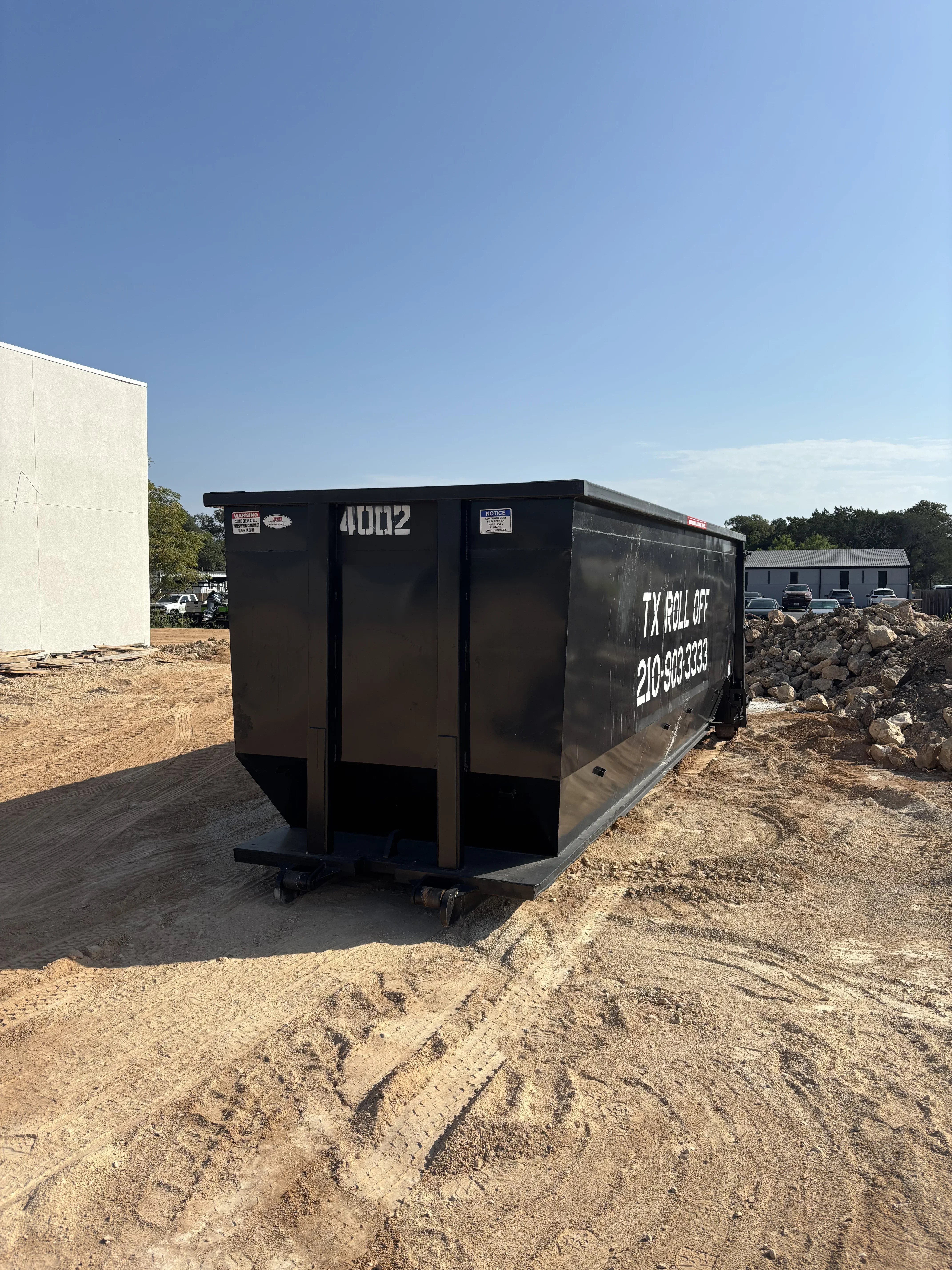 Black steel roll-off dumpster on construction site with dirt and stone aggregate